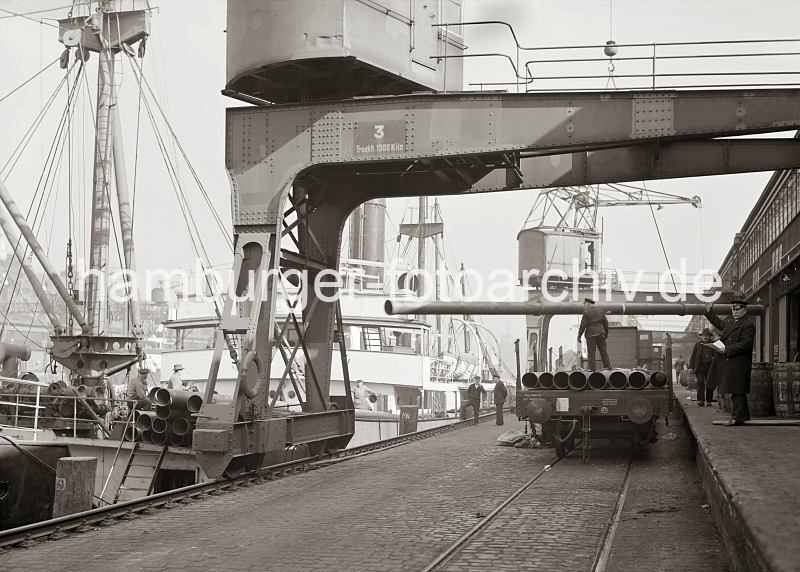 Historische Hafenmotive - Verladung von Eisenrohren auf ein Frachtschiffe - Kaiserkai, Sandtorhafen - Hamburgerhafenbilder auf Foto-Leinwand oder Posterprints.  02185_723a Am Haken des Halbportalkrans hngt ein langes Eisenrohr, das gerade von einem offenen Gterwaggon abgeladen worden ist. An Deck des Frachters am Kaiserkai sind weitere Rohre gelagert.