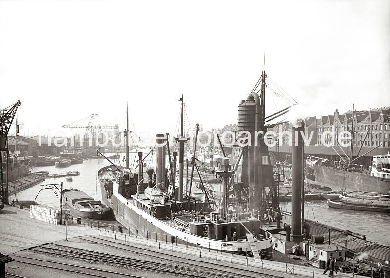 Hamburger historische Hafenmotive aus dem Bildarchiv der HHLA - Getreideheber und Kohlenheber im Sandtorhafen, Massengutfrachter. Hamburgbilder auf Foto-Leinwand oder Posterprints. 02193_0079 Ein Massengutfrachter hat mit dem Heck am Kai im Sandtorhafen fest gemacht - auf der steuerbordseite liegt ein pneumatischer Getreideheber, der das Getreide mittels eines Luftstroms ber die Saugleitungen aus dem lngsseits liegenden Binnenschiffs in ein Behltnis des Hebers befrdert. Von dort wird das Getreide ber ein Auslaufrohr in den Laderaum des Dampfers geschttet.  Im Hintergrund liegt am Kaiserkai ein Kohlenheber. 02194_78_getreideheber_frachtschiff_massengutfrachter.html