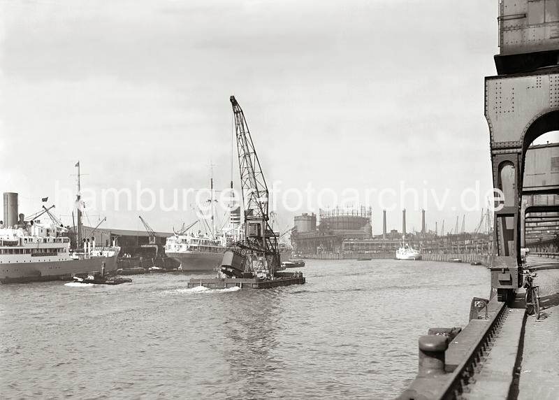 02234_750a Der Schwimmkran hat den verunglckten Rollkran an Deck gehievt und fhrt mit eigenem Antrieb durch den Baakenhafen Richtung Elbe. Im Hintergrund das Gasometer und die Schornsteine der Hamburger Gasanstalt auf dem Groen Grasbrook. Historische Hafenfotografien Hafen Hansestadt Hamburg; Schwimmkran im Baakenhafen - Versmannkai, Petersenkai; ca. 1932. 