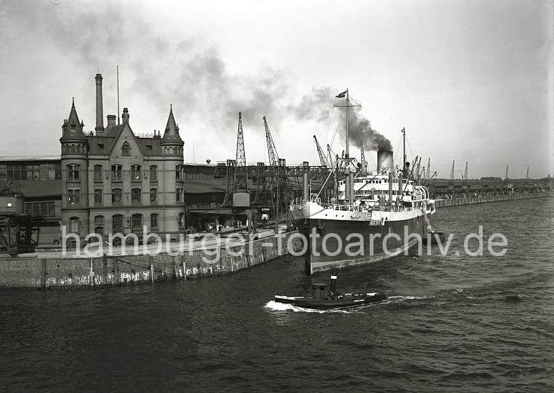 02235_152 Blick ber den Magdeburger Hafen zum Versmannkai des Hamburger Baakenhafens. Der Dampfer NATIA hat am Kai fest gemacht -  Qualm steigt aus seinem Schornstein. Auf der Kaianlage transportieren Kaiarbeiter Fruchtkisten mit der Sackkarre in den Fruchtschuppen A - eine Hieve Kisten wird vom Kran auf der Rampe abgesetzt. Fruchtschuppen A am Versmannkai des Baakenhafen - Frachtschiff; ca. 1935.