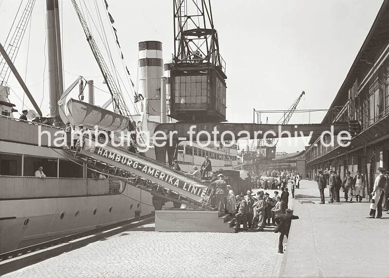 Historische Hamburgbilder des Hamburger Hafens. Passagiere gehen an Bord eines Schiffs der Hamburg Amerika Linie im Baakenhafen. 02246_759 Am Versmannkai besteigen Passagiere die Gangway eines Passagierschiffs der Hamburg-Amerika-Linie HAPAG. Unter dem Halbportalkran stehen die LKW mit dem Gepck der Amerikareisenden, ein Arbeiter wartet darauf, die Koffer an Bord des Dampfers tragen zu knnen. Auf der Laderampe stehen Kaiarbeiter des Fruchtschuppens und beobachten das Geschehen.