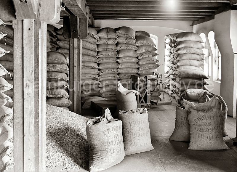 505_505a Der Kaffee aus Kolumbien ist in Jutescke vernht und bis an die Decke des Speicherbodens gestapelt. Die Scke tragen die Aufschrift Produkt of Colombia - 70 Kilos. Ein Haufen Kaffee ist auf dem Lagerboden ausgeschttet - im Hintergrund eine Waage, mit der die Scke gewogen werden.