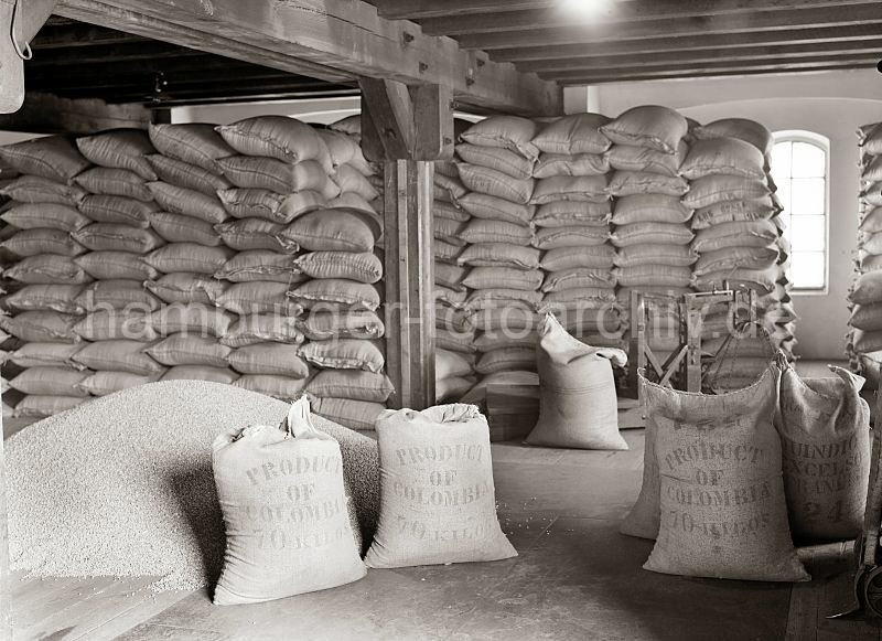 506_505 Der Kaffee aus Kolumbien ist in Jutescke vernht und bis an die Decke des Speicherbodens gestapelt. Die Scke tragen die Aufschrift Produkt of Colombia - 70 Kilos. Ein Haufen Kaffee ist auf dem Lagerboden ausgeschttet - im Hintergrund eine Waage, mit der die Scke gewogen werden.