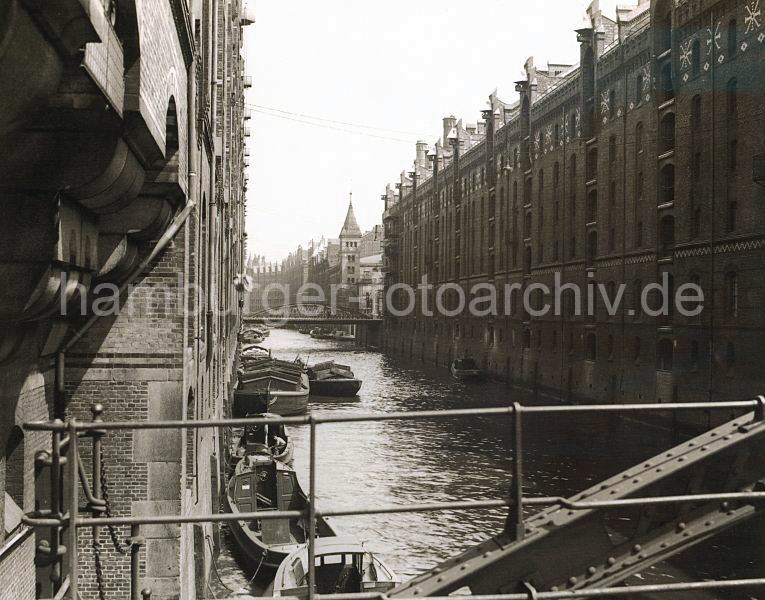 507_061_15 Blick von der Kehrwiederstegbrcke auf das Brooksfleet; Schuten und Barkassen liegen an der Gebudemauer des Speichergebudes Block D. Die Kaffeeladung eines der Khne wird gerade gelscht. Eine Hieve Scke wird mit der Winde, die sich unter dem Dach des Speichers befindet auf den Lagerboden gebracht. Auf der rechten Fleetseite die neogotischen Backsteinfassaden der Speicherblcke L, M, N und O - im Hintergrund die Kibbelstegbrcke. 