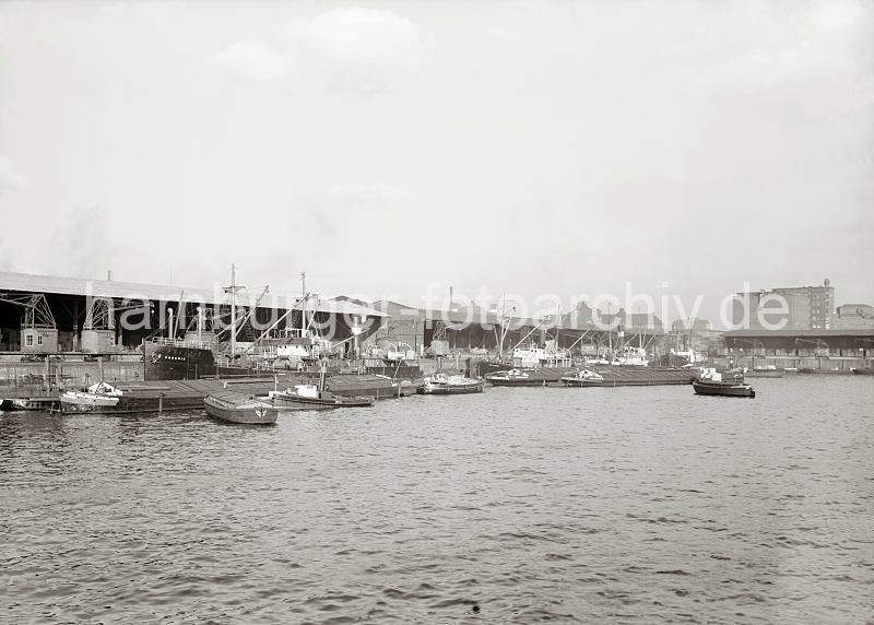 Hafenbilder von der Hansestadt Hamburg - Fotoarchiv der HHLA: Frachtschiffe und Schuten am Dalmannkai - Khlhaus am Hbenerkai. 603_11_678a Blick ber das Hafenbecken des Grasbrookhafens zum Dalmannkai; u.a. haben dort die Frachter PROCRIS und CITY OF BREMEN fest gemacht. Binnenschiffe und Schuten liegen lngsseits, der Schlepper GRETE zieht einen Lastkahn an seine Position. Vor den Lagerschuppen 14 + 15 fahren Hafenkrane auf Schienen. Im Hintergrund ist links die Fassade und der hohe Schornstein des Kaispeichers B zu erkennen, gefolgt von den Gebuden des Amts fr Strom- und Hafenbau und rechts das 1928 nach dem Entwurf des Oberbaudirektors Fritz Schumacher errichtete Khlhaus.